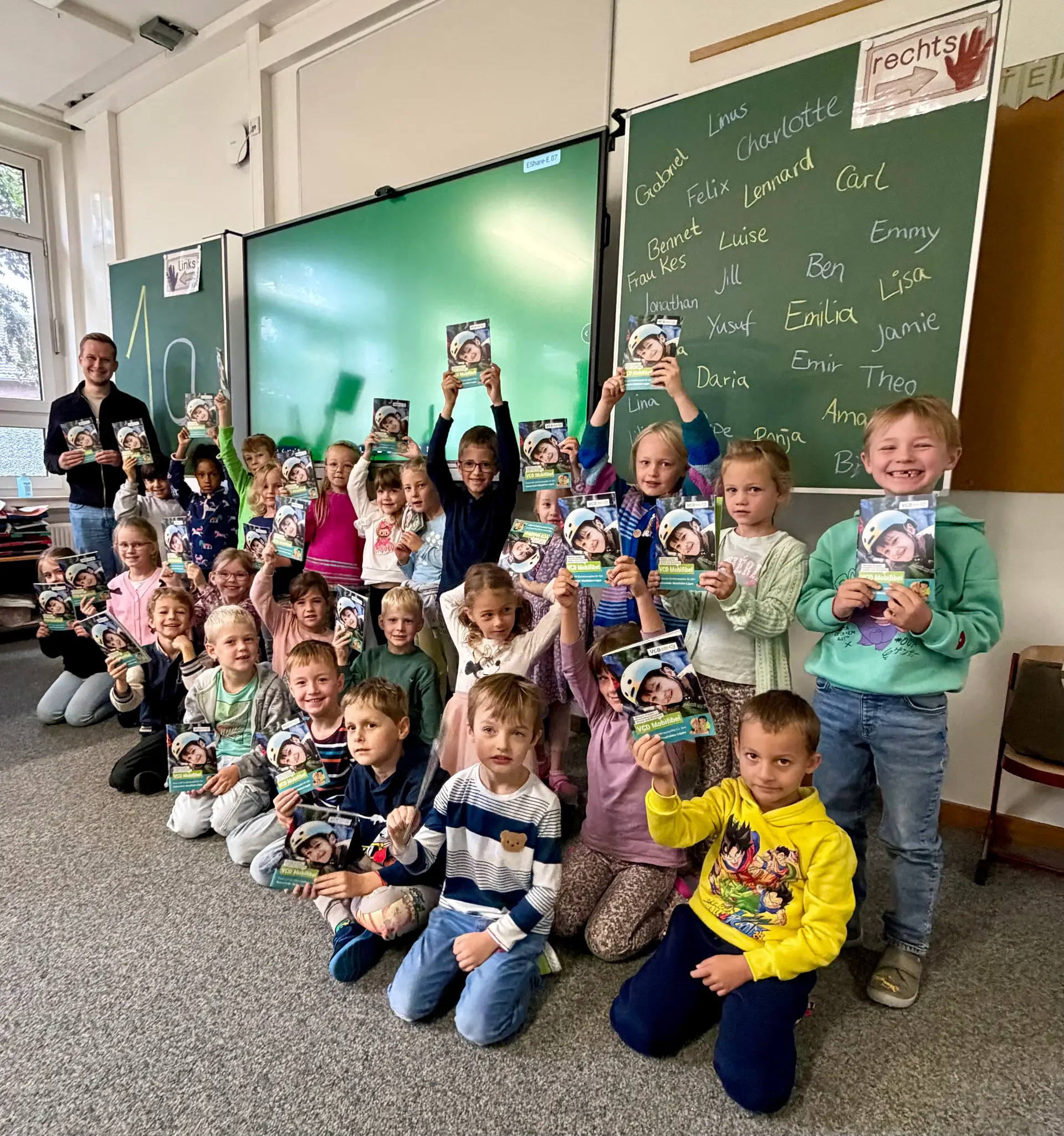 Kinder halten eine Mobifibel im Umfeld der Marienschule, zur Verteilung der Broschüre für sichere und klimafreundliche Schulwege.